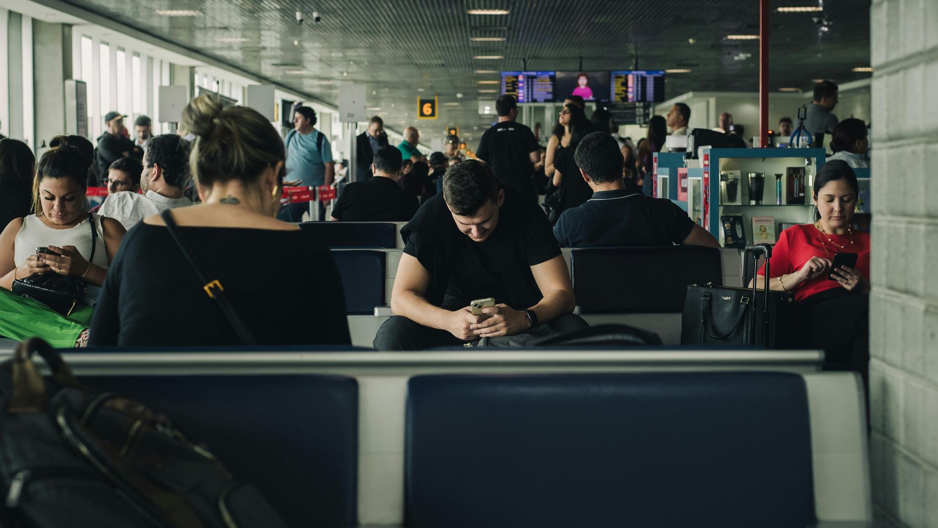 Travelers seated and waiting at São Paulo airport terminal, engaging with smartphones.
