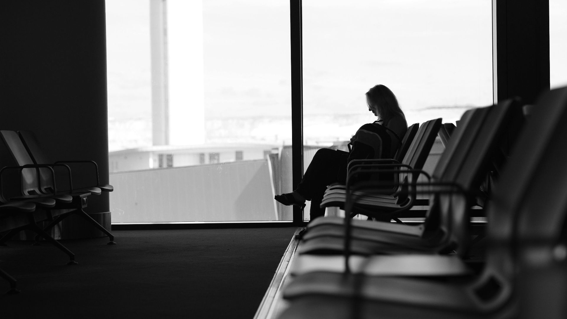 Silhouette of a woman sitting in an airport terminal lounge, with view of control tower.
