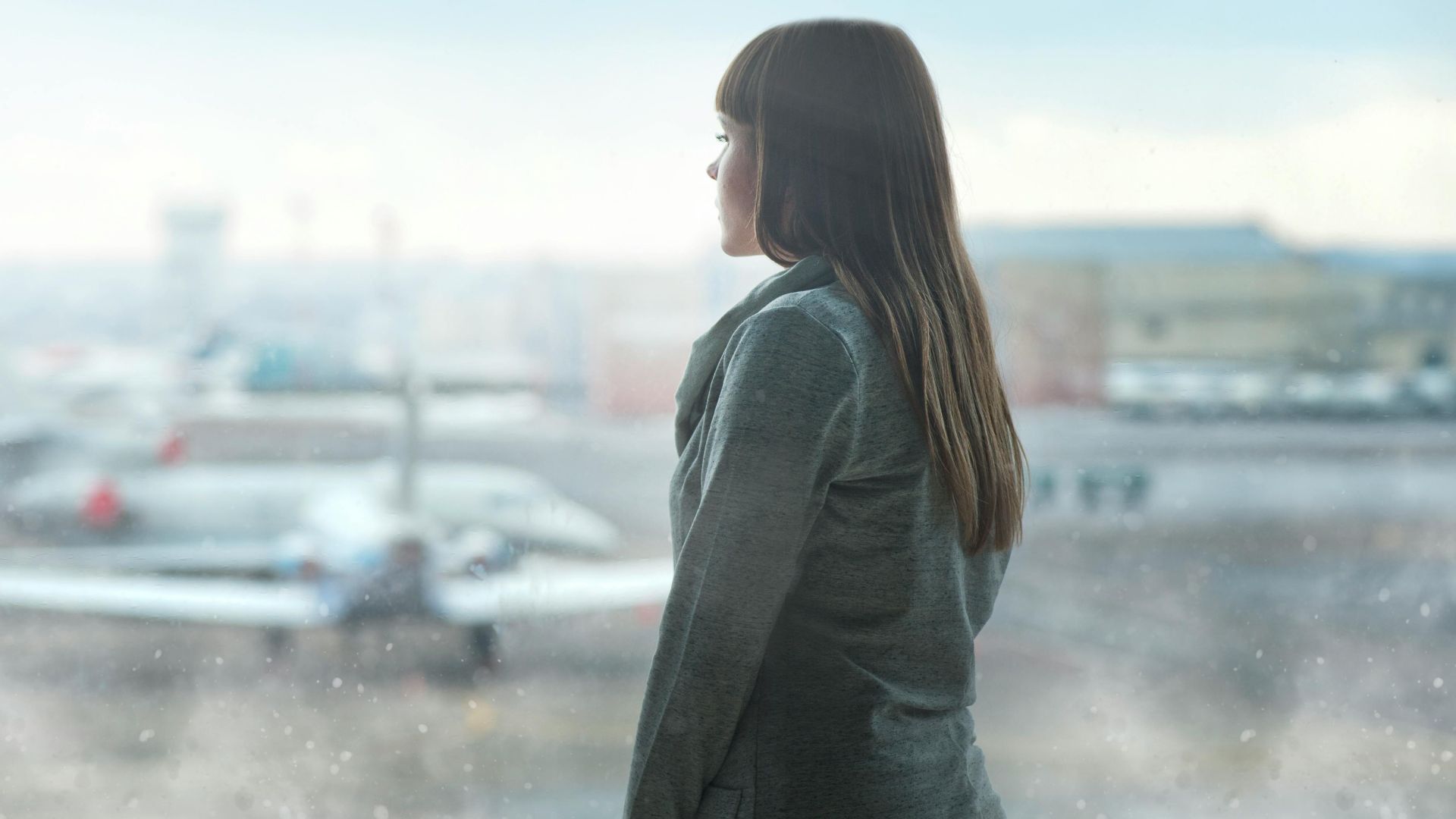 A woman gazing at airplanes through a window at Kyiv's airport terminal, capturing a moment of reflection.