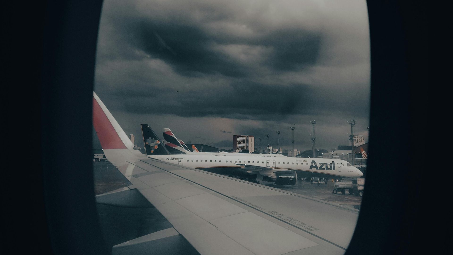 View from airplane window showing wing and stormy clouds at airport.
