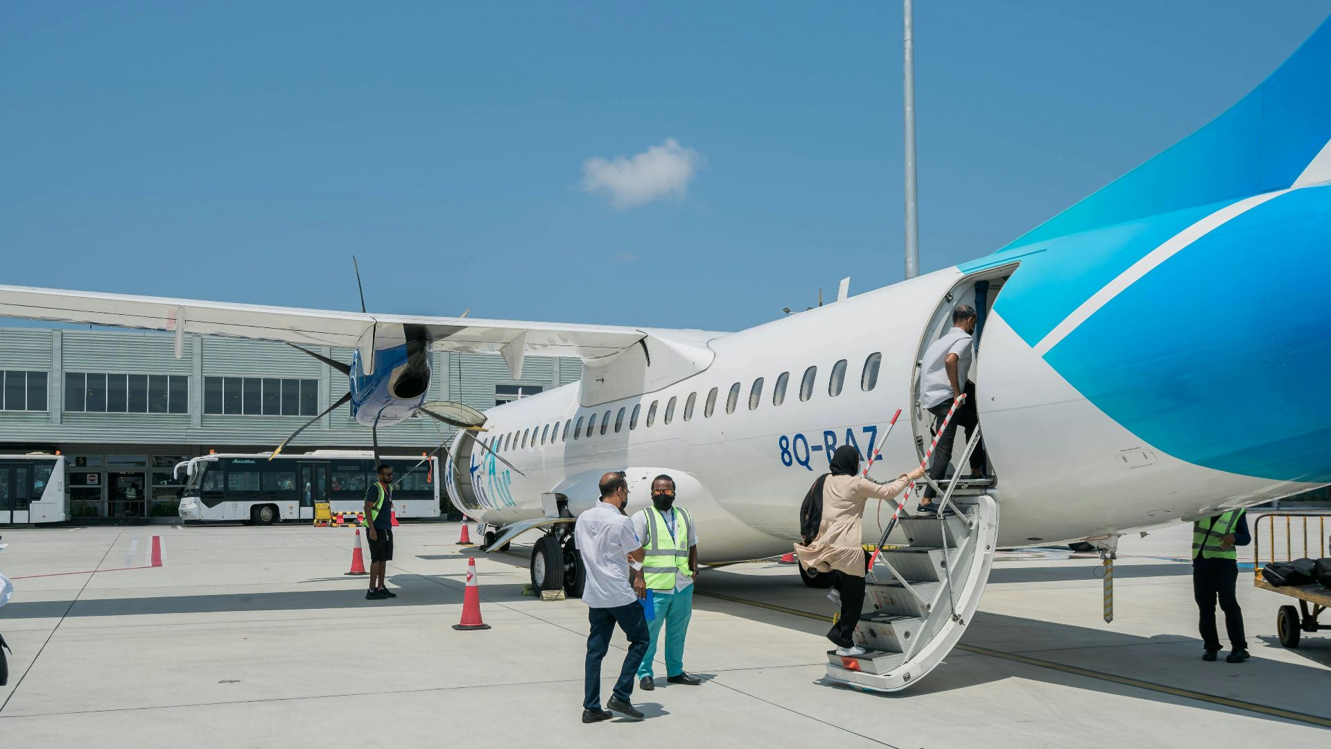 Passengers board a blue and white ATR 72 aircraft at an airport under clear skies.