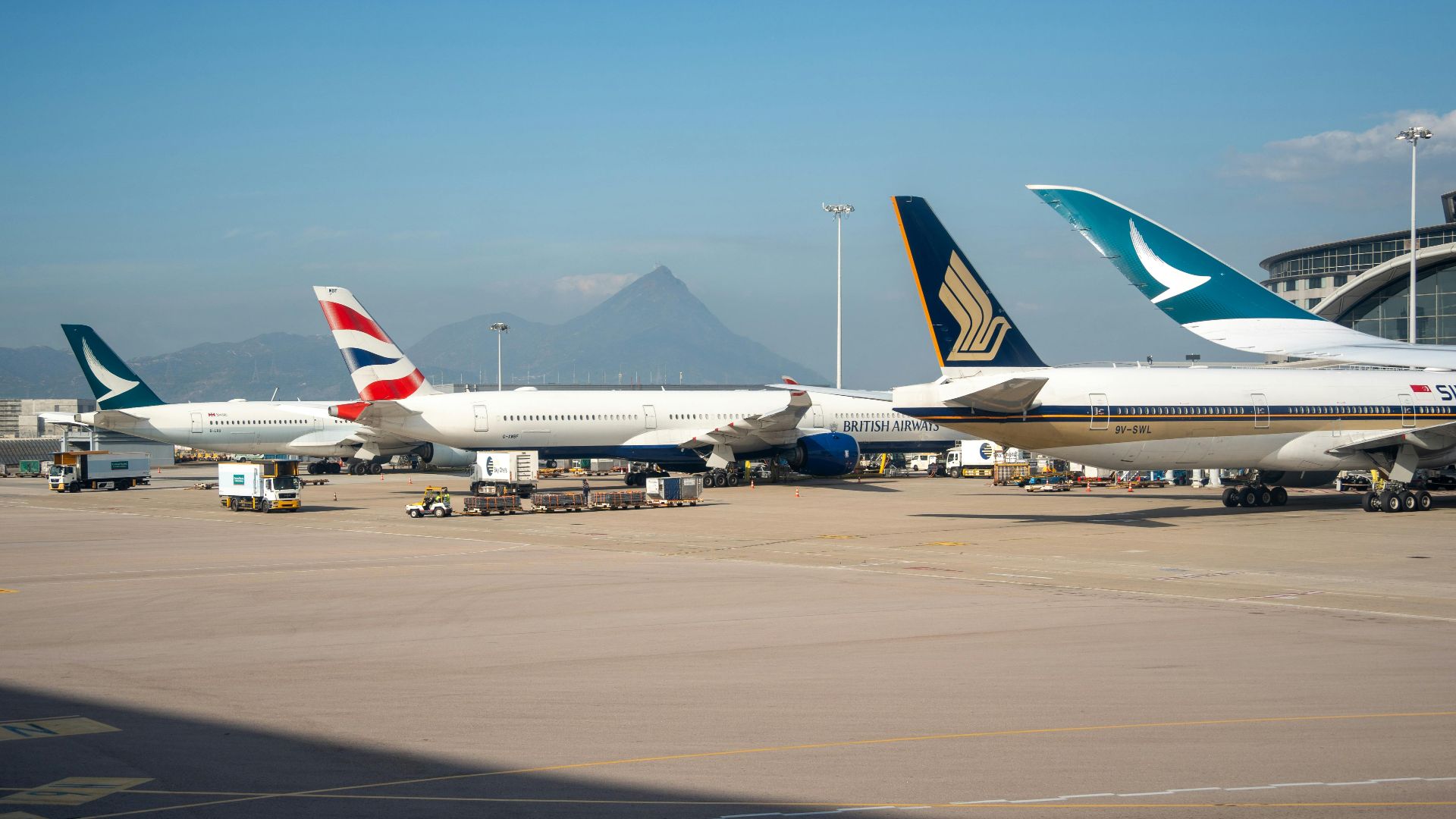 Multiple commercial airplanes parked at an airport terminal with a mountain view in the background.