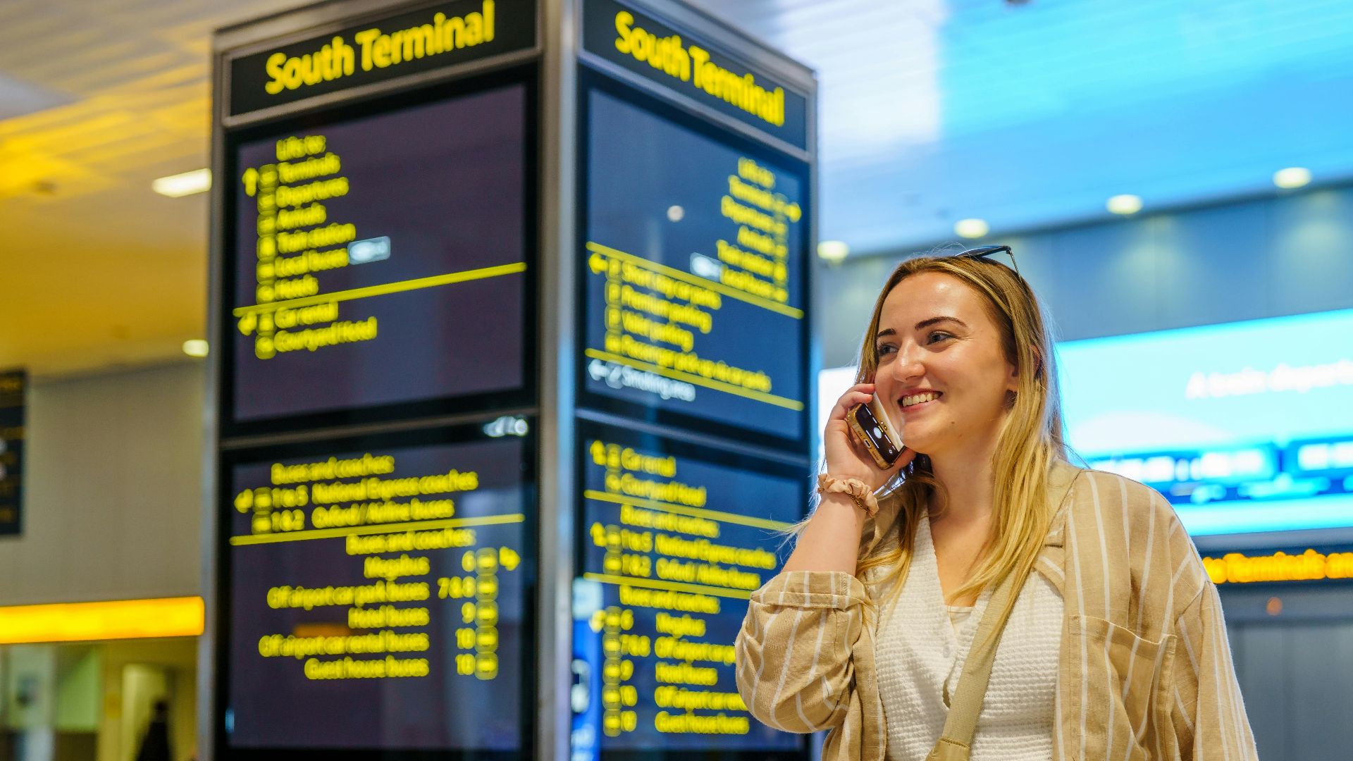 Smiling woman on phone in South Terminal of Gatwick Airport, Horley, enjoying her travel experience.