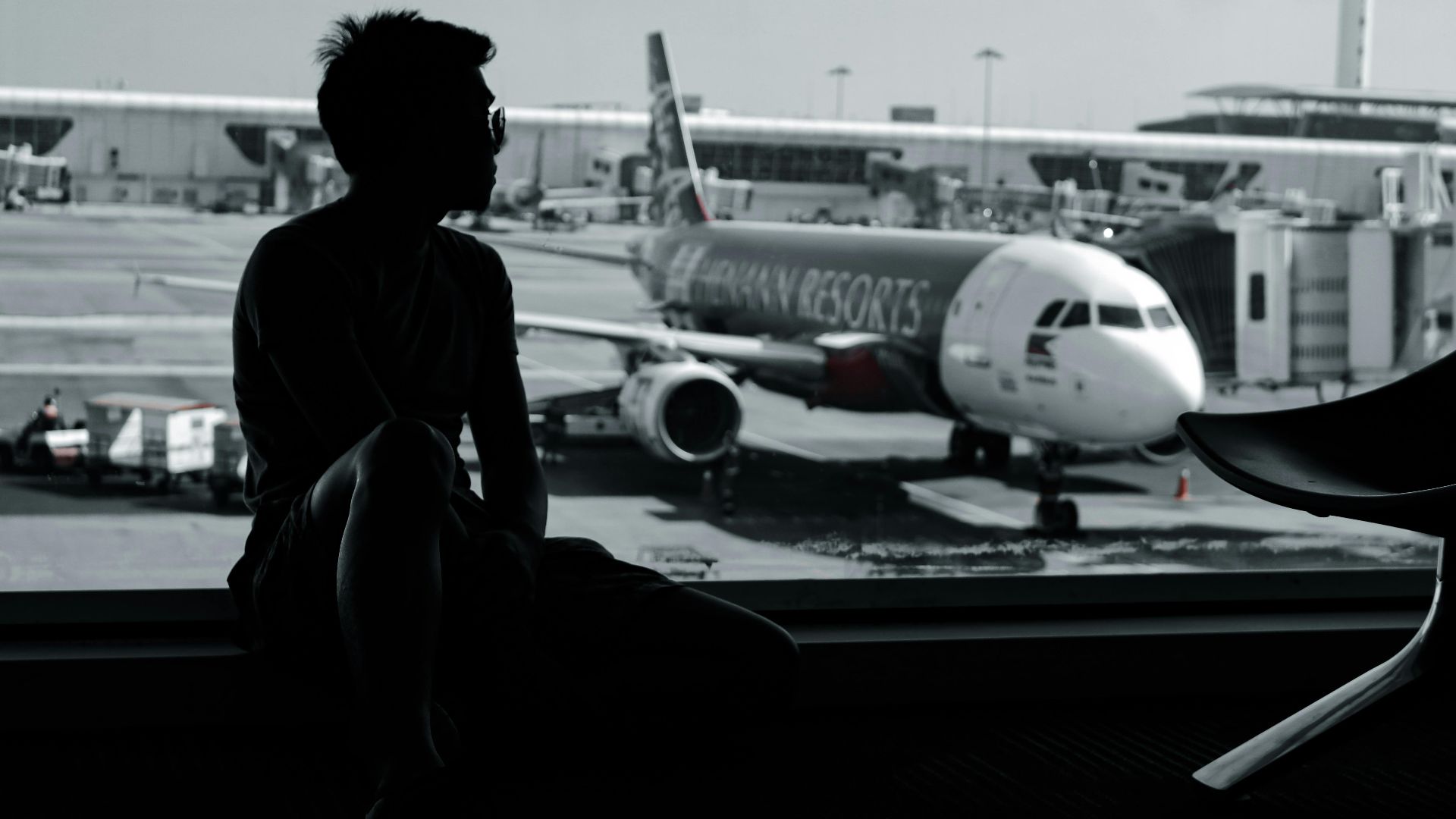 A silhouetted man sits in an airport terminal, viewing an airplane on the tarmac.