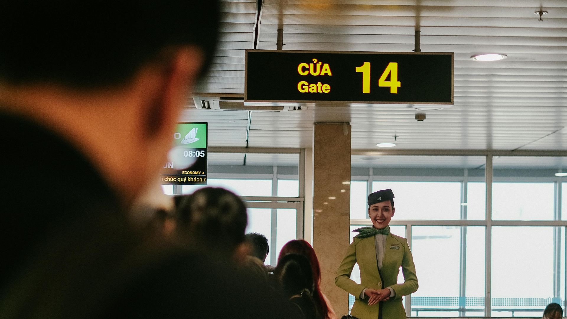 Flight attendant at airport gate 14, Vietnam, offering guidance to passengers indoors.