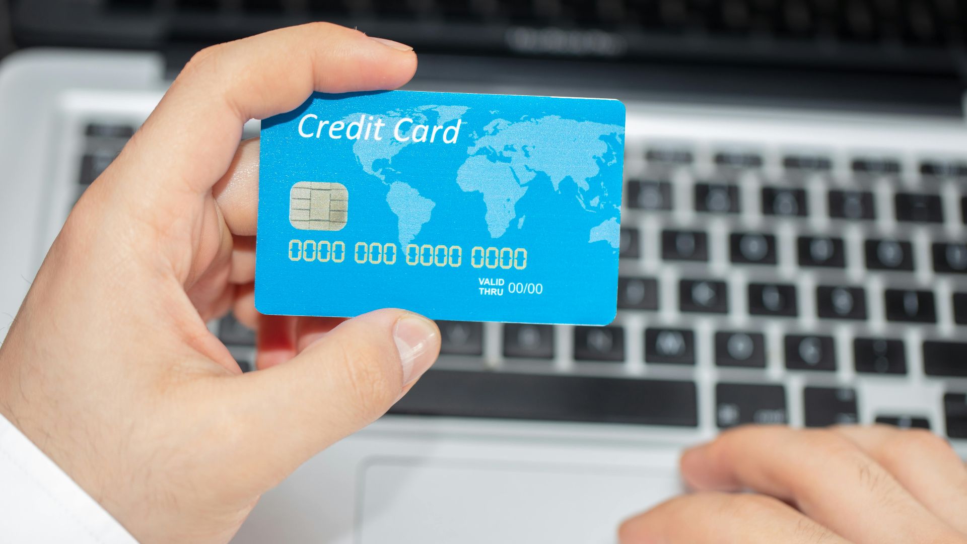 Person holding credit card near laptop for online shopping, emphasizing secure online transactions.