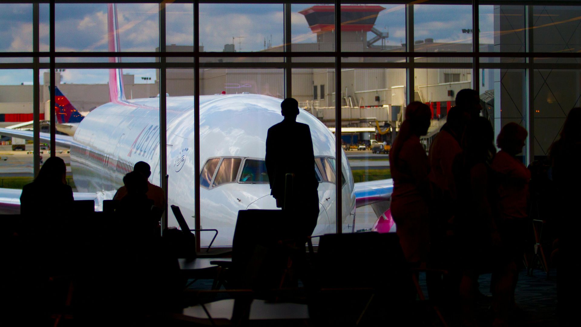 Silhouettes of travelers waiting at an airport terminal with an airplane visible through the window.