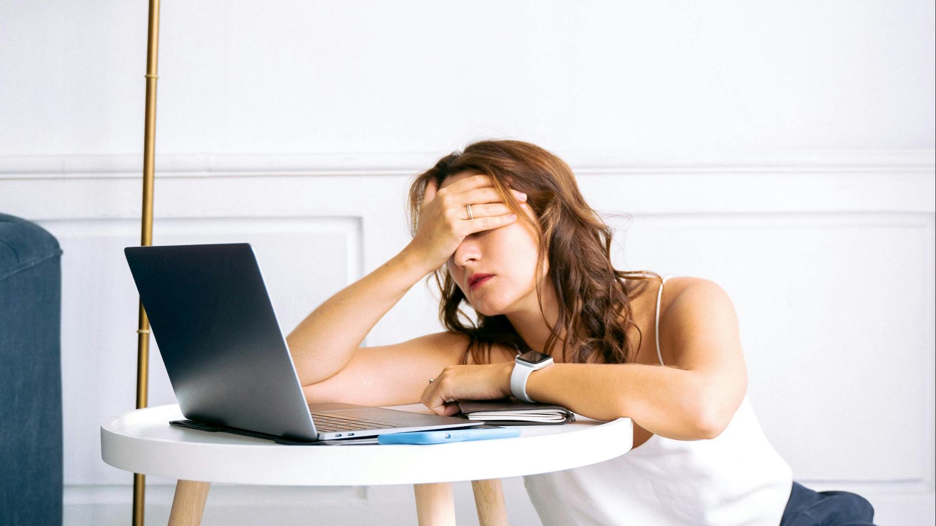 A woman showing signs of fatigue while working remotely at a laptop indoors.