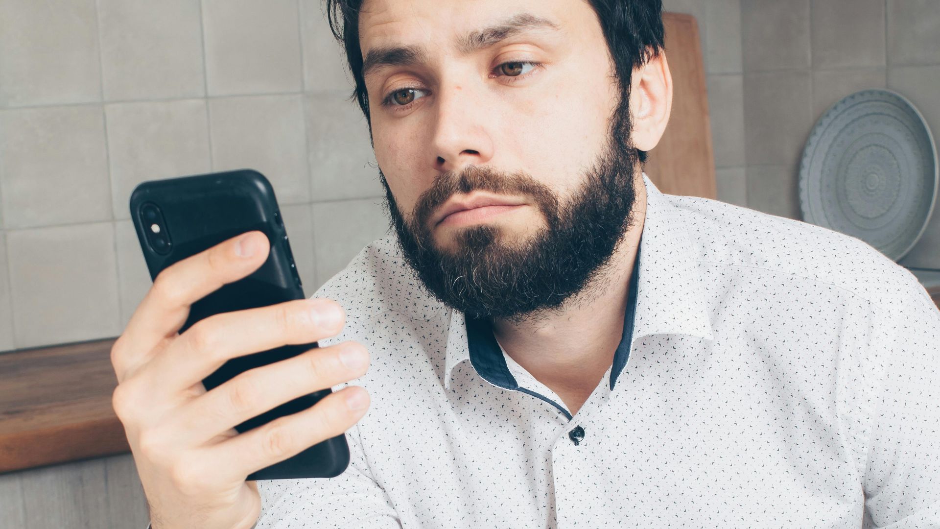 A man looks frustrated while checking his smartphone, possibly experiencing a banking issue or scam.