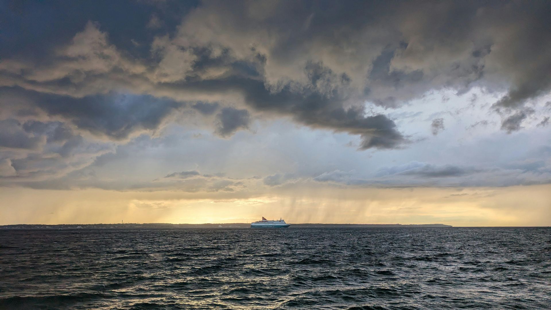 A cruise ship sails under stormy skies at sunset, capturing a dramatic and serene ocean scene.