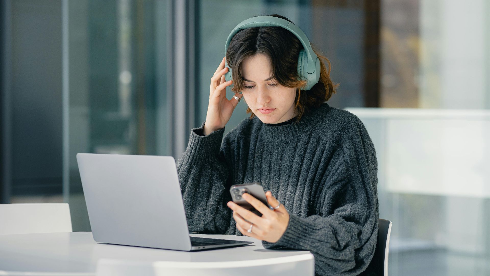 Focused young woman with headphones using laptop and smartphone in a modern cafe.