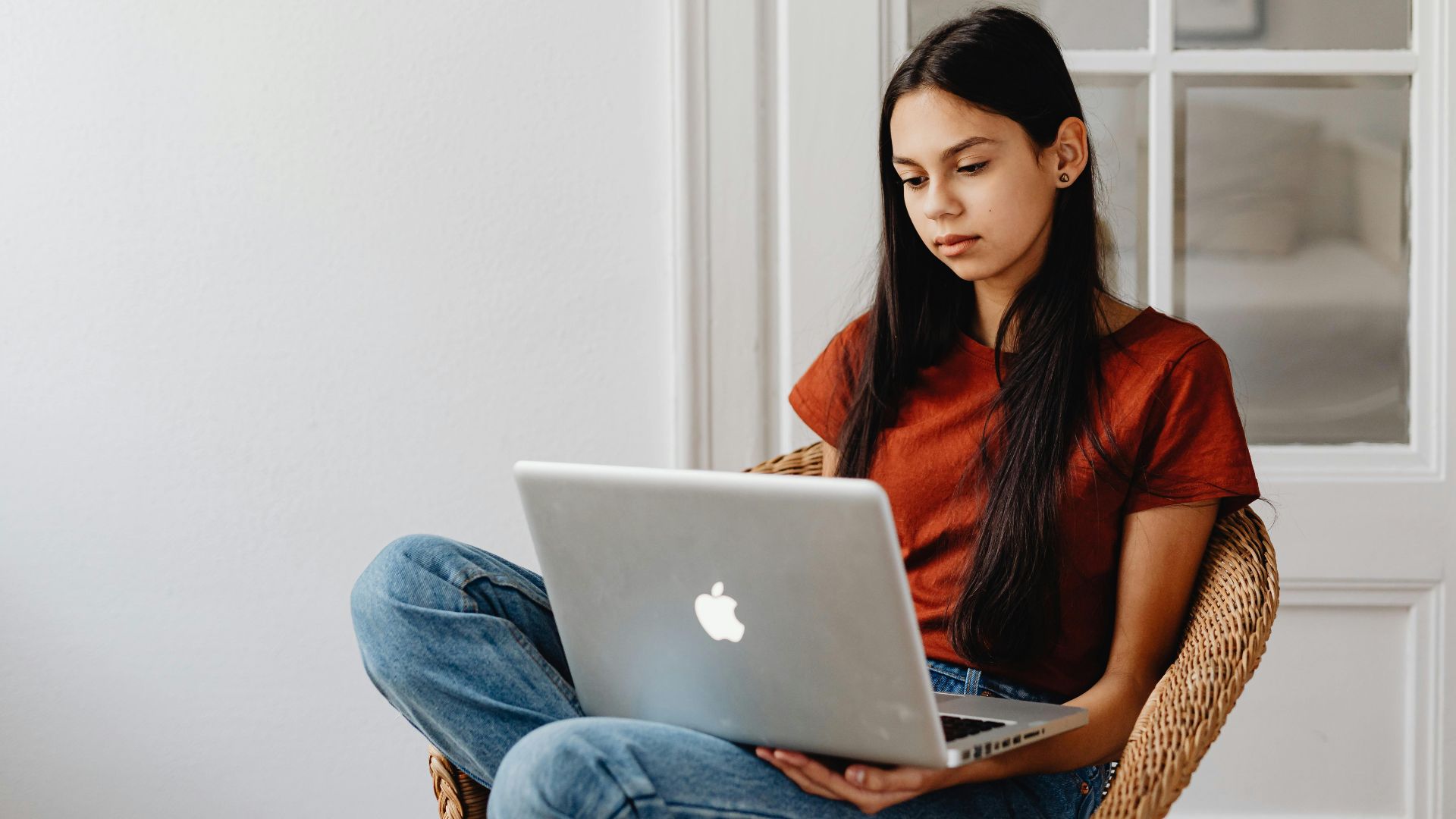 A teenage girl sits comfortably while using a laptop indoors.