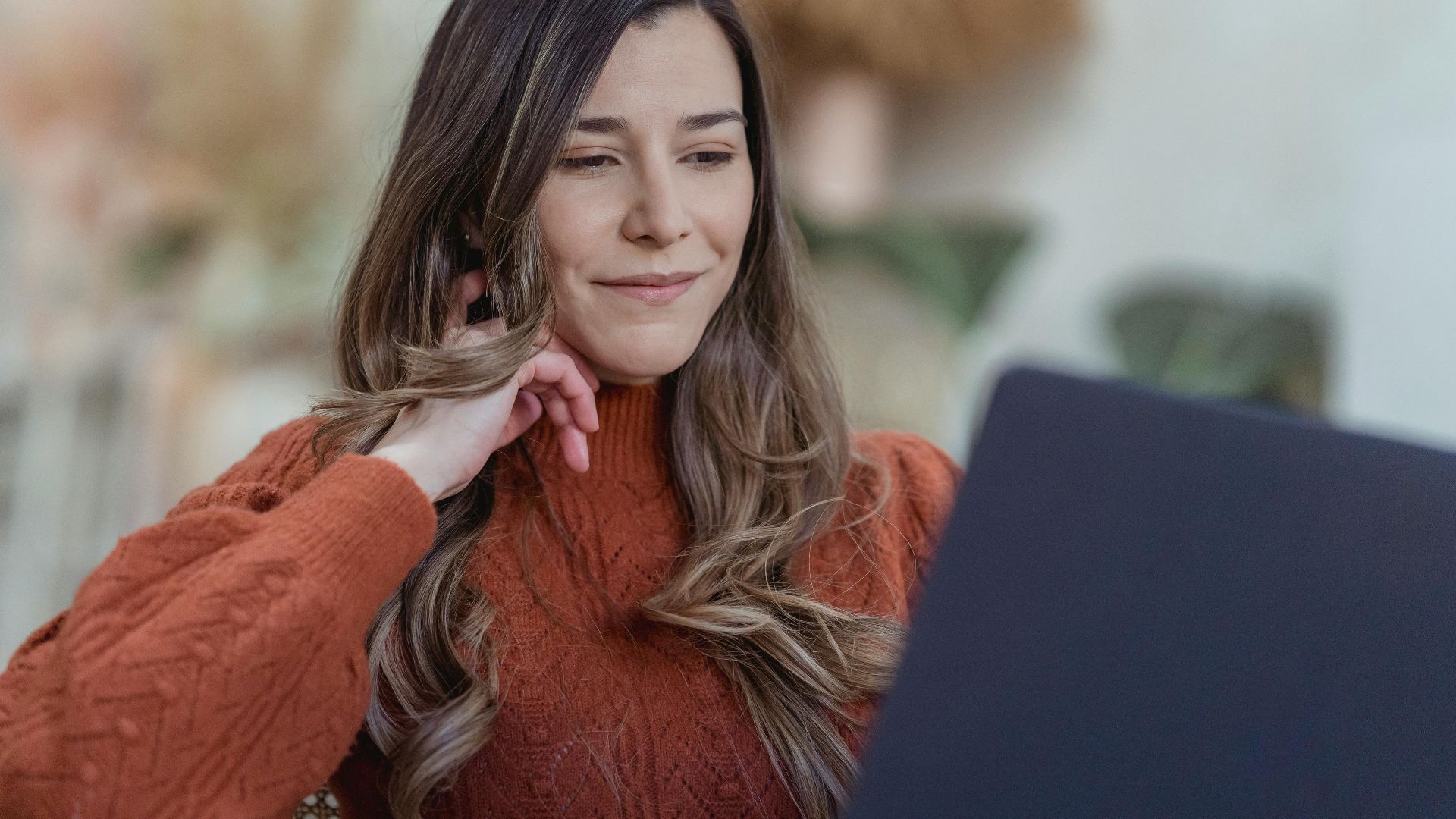 Low angle of positive female remote worker touching cheek while browsing laptop for remote project