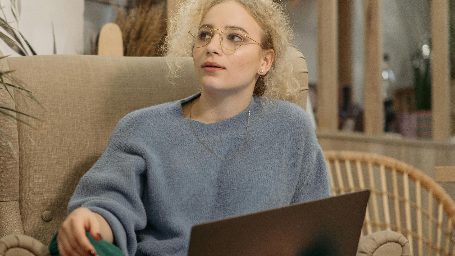 Woman in cozy setting with laptop and coffee on armchair indoors.
