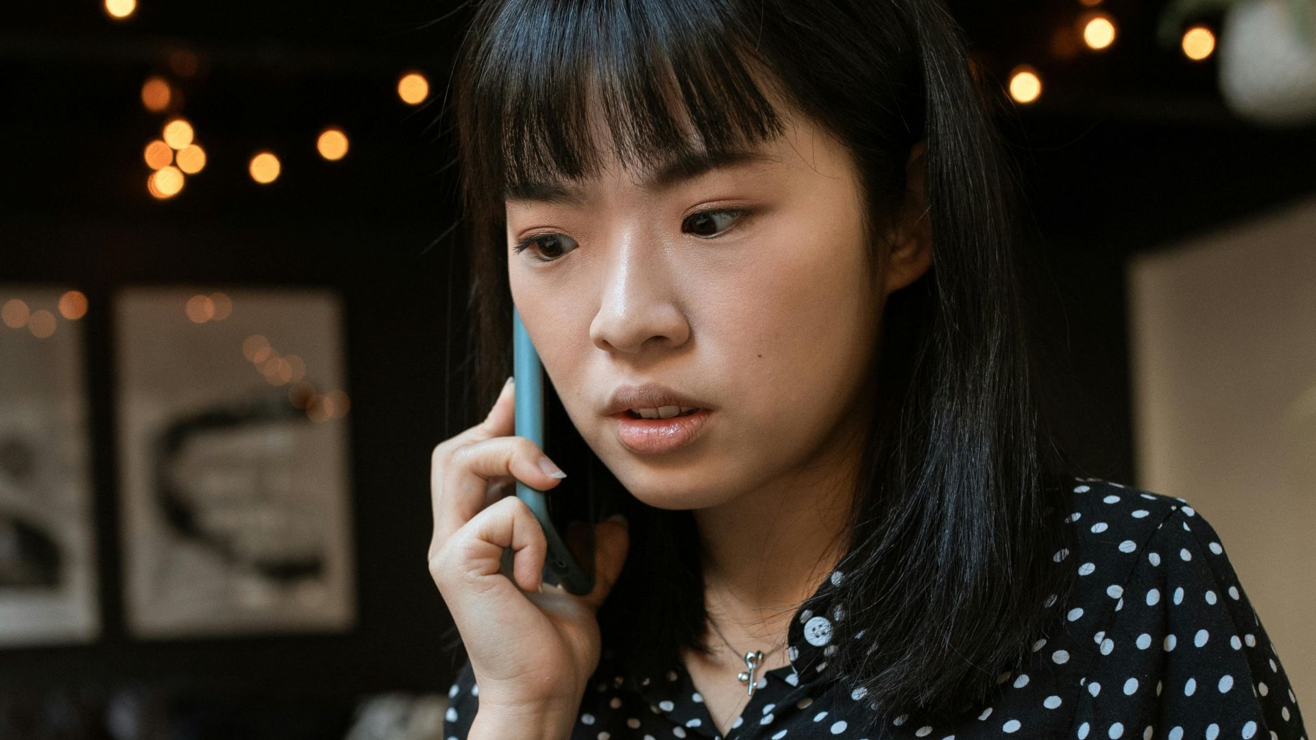 Focused young woman in a polka dot blouse taking a call indoors.