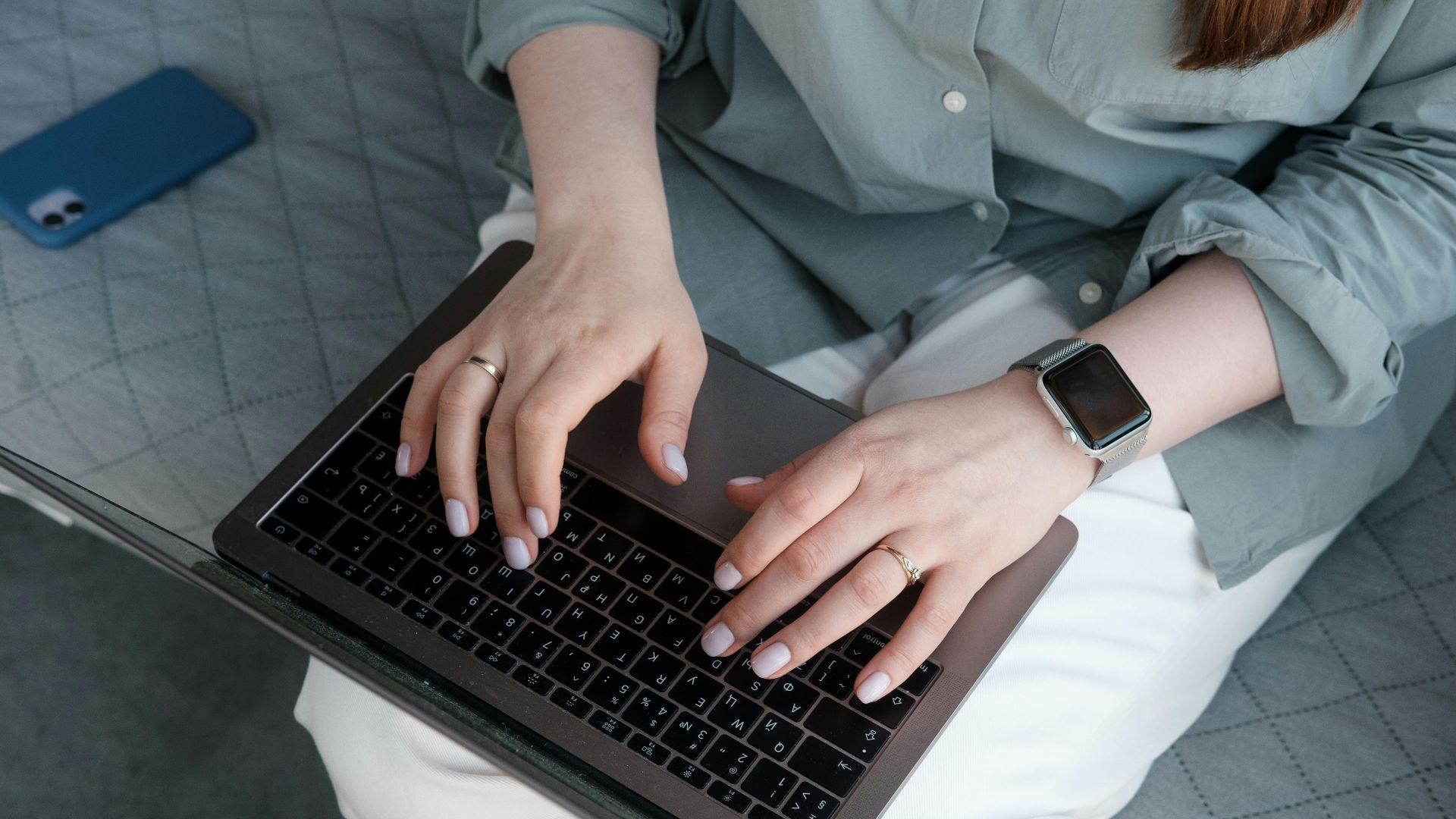 Close-up of a woman typing on a laptop while wearing a smartwatch and rings, indoors.