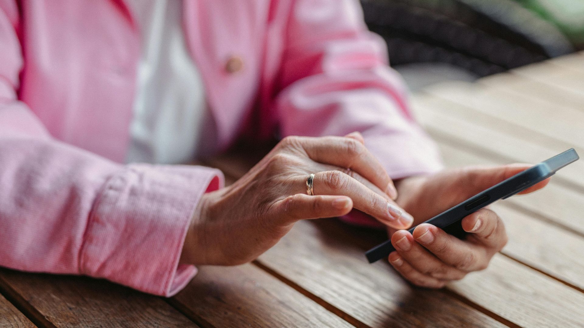 A person in pink sleeves texting on a smartphone with a wooden table background.