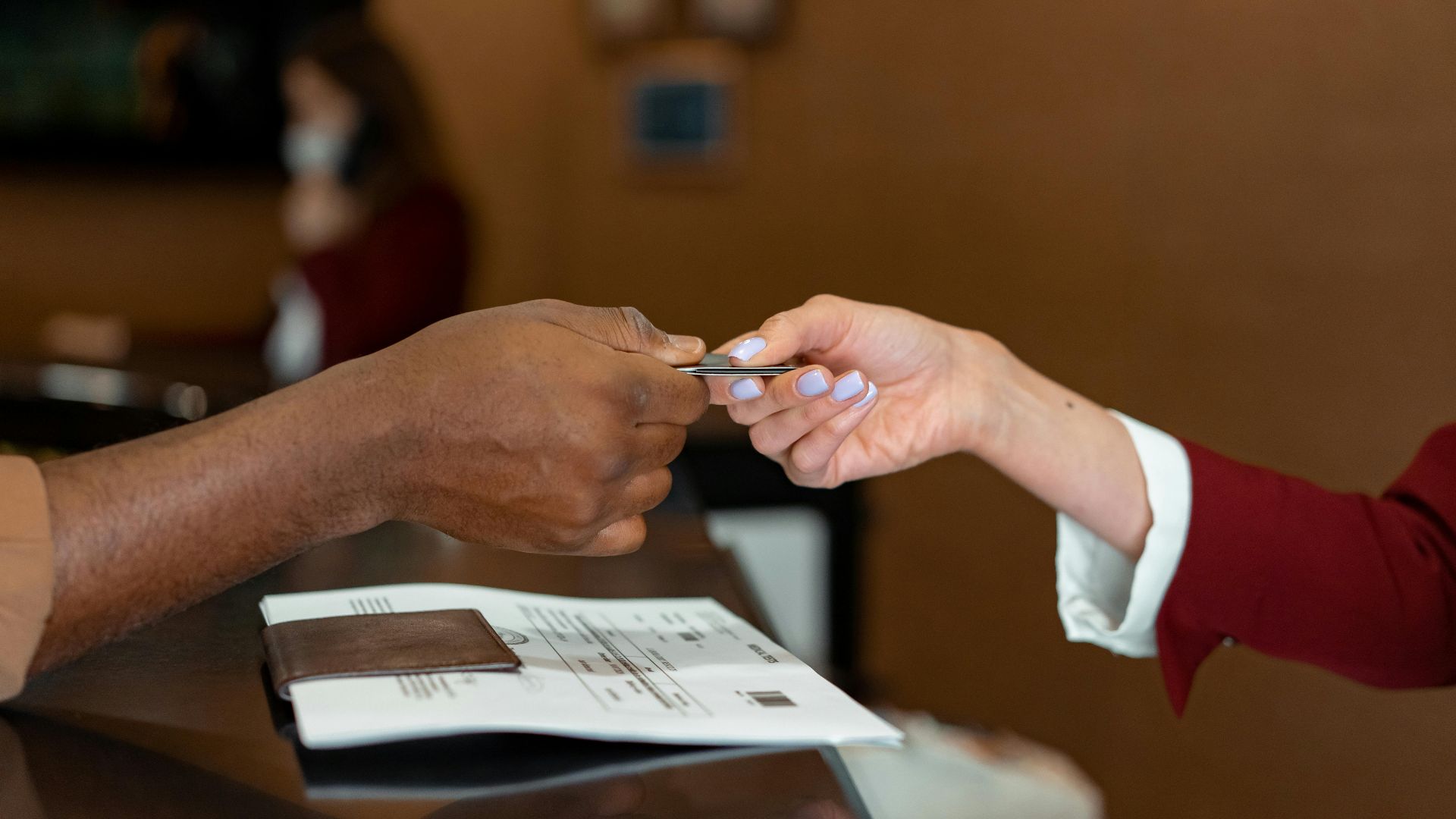 Close-up of a hotel receptionist receiving a credit card from a guest, highlighting a transaction at check-in.