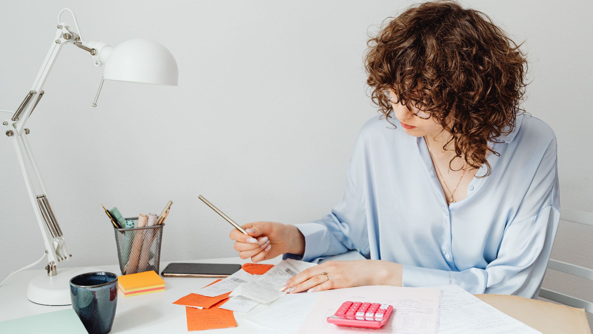 Woman in office calculating expenses with documents, calculator, and coffee.