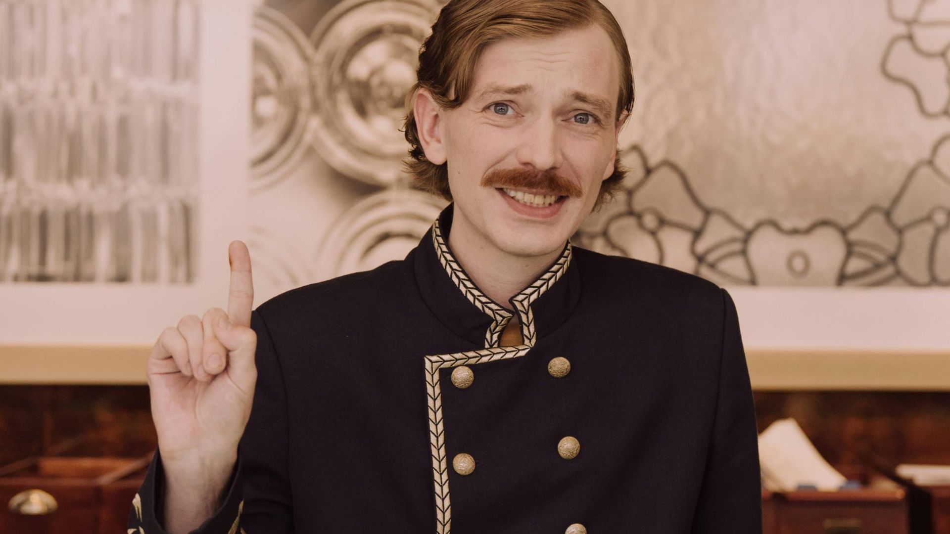 Friendly hotel concierge in uniform smiling and welcoming guests at the reception desk.