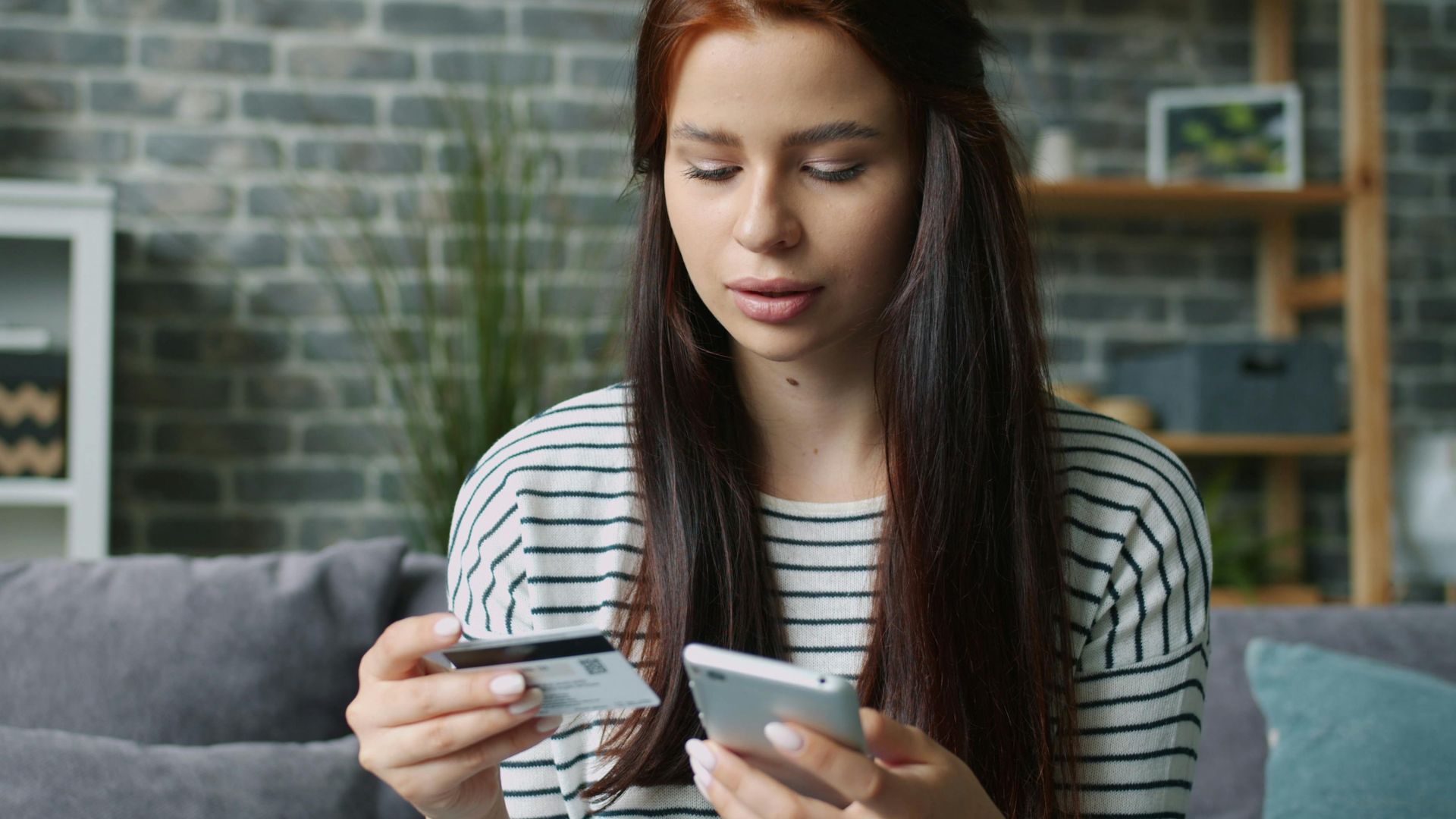 Woman using smartphone and credit card for online shopping in living room.
