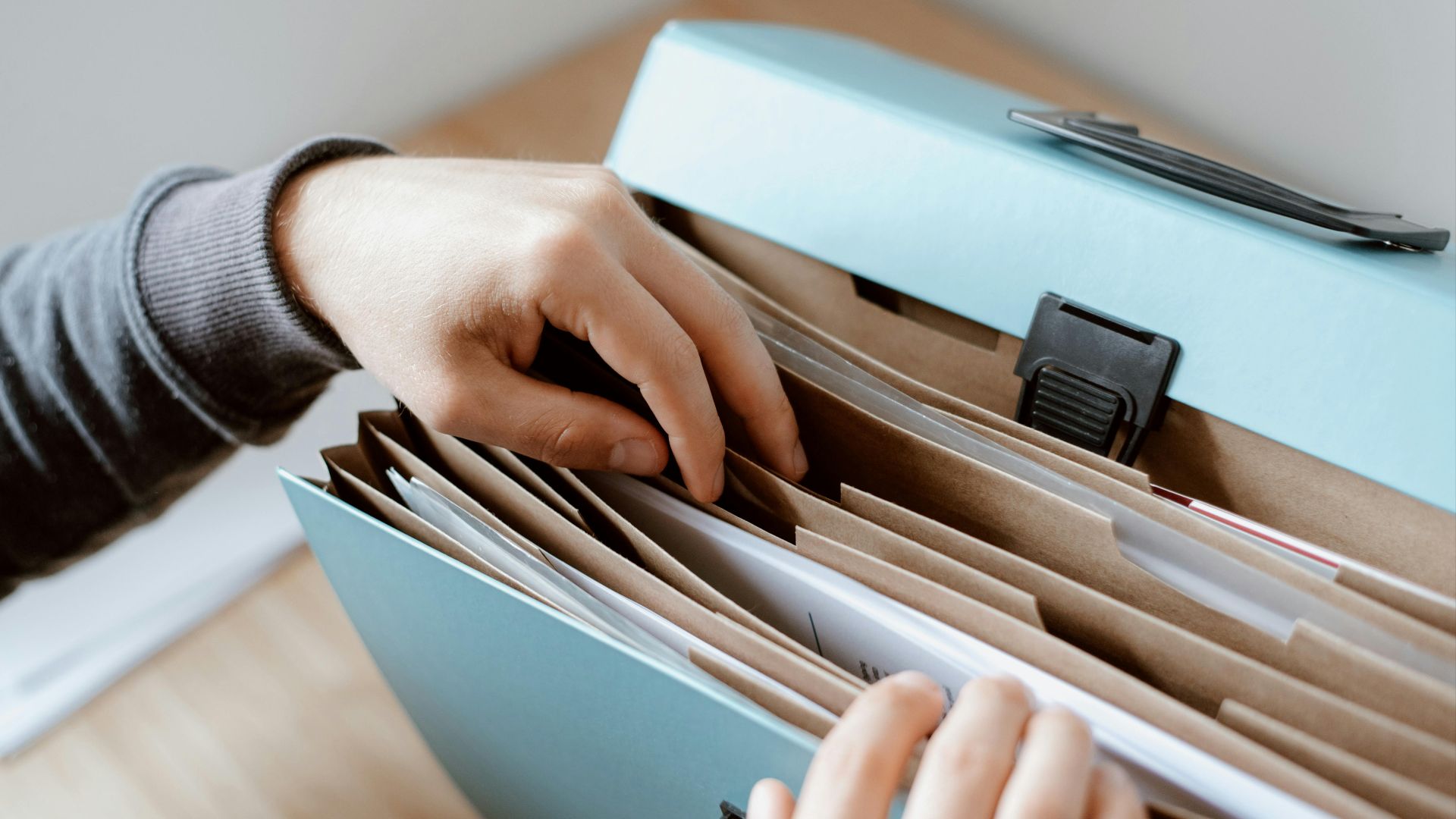 Crop unrecognizable person selecting document in opened briefcase for documents placed on wooden table