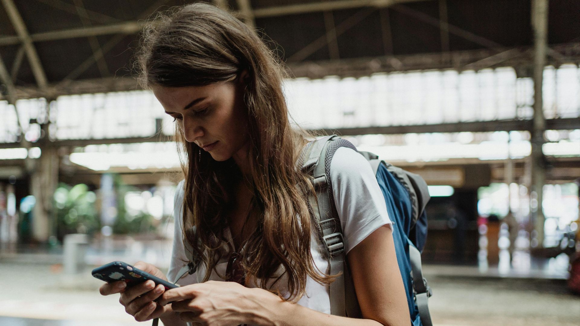 A young woman checks her smartphone while traveling at a train station.