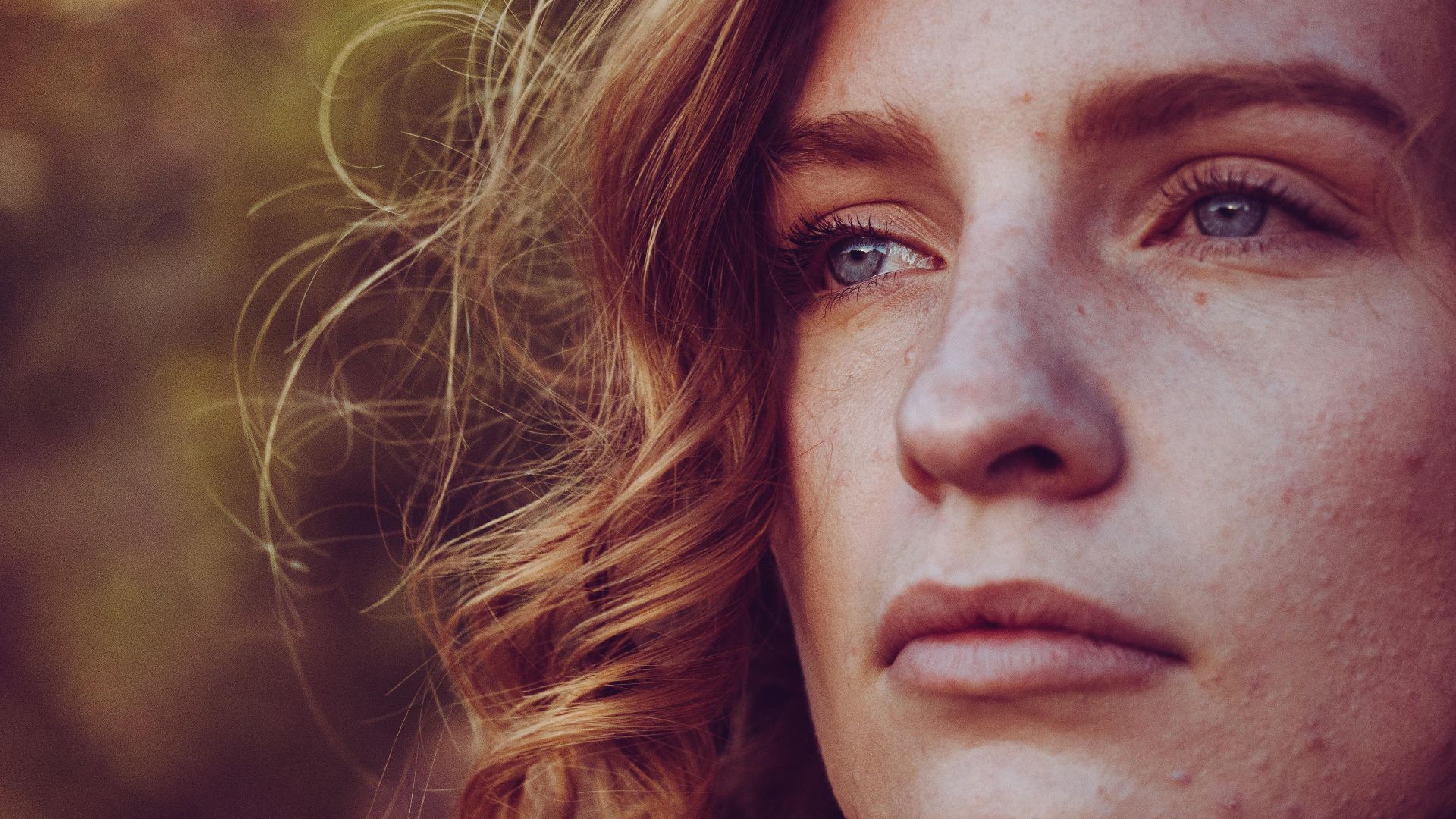 Close-up portrait of a young woman with curly hair and blue eyes, exuding calmness.