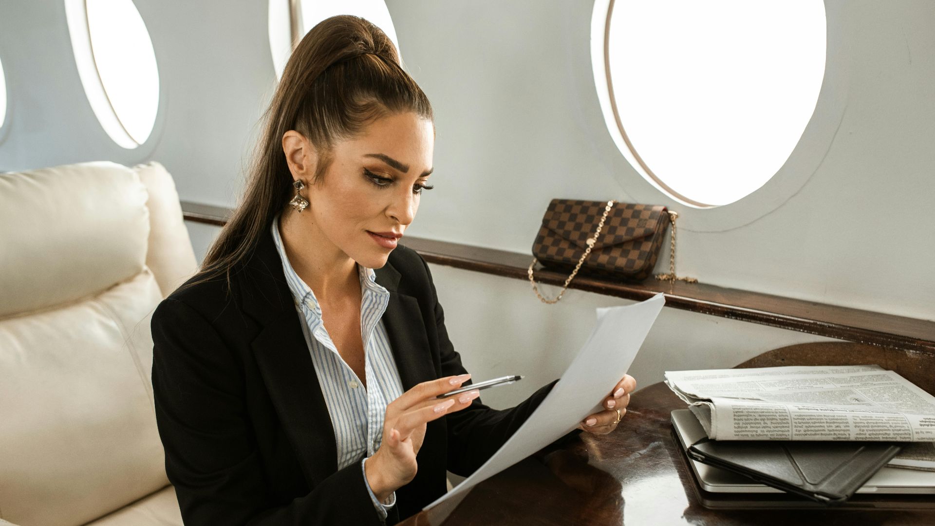 Woman in formal attire reviewing documents on a private jet. Luxurious air travel setting.