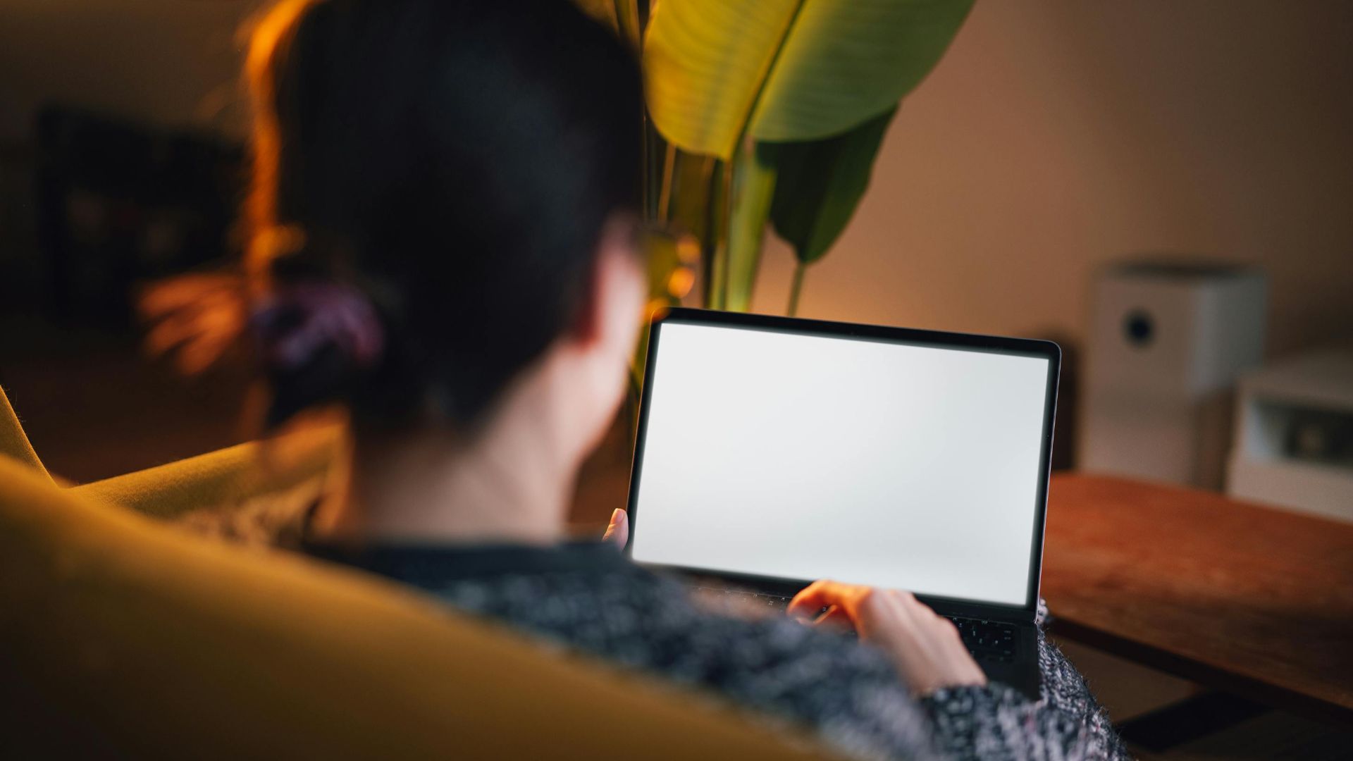 A woman using a laptop in a comfortable home setting, showcasing a relaxed and focused work environment.