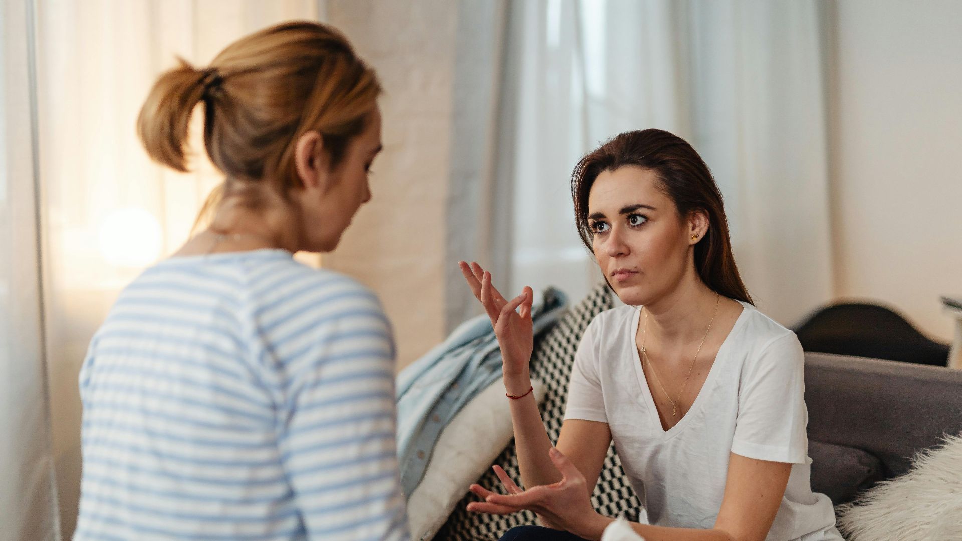 Two women sitting on a sofa, engaged in a serious discussion at home.