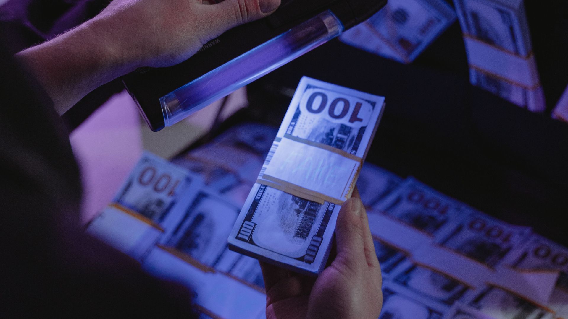 A person examining hundred dollar bills under UV light in a briefcase, ensuring authenticity.