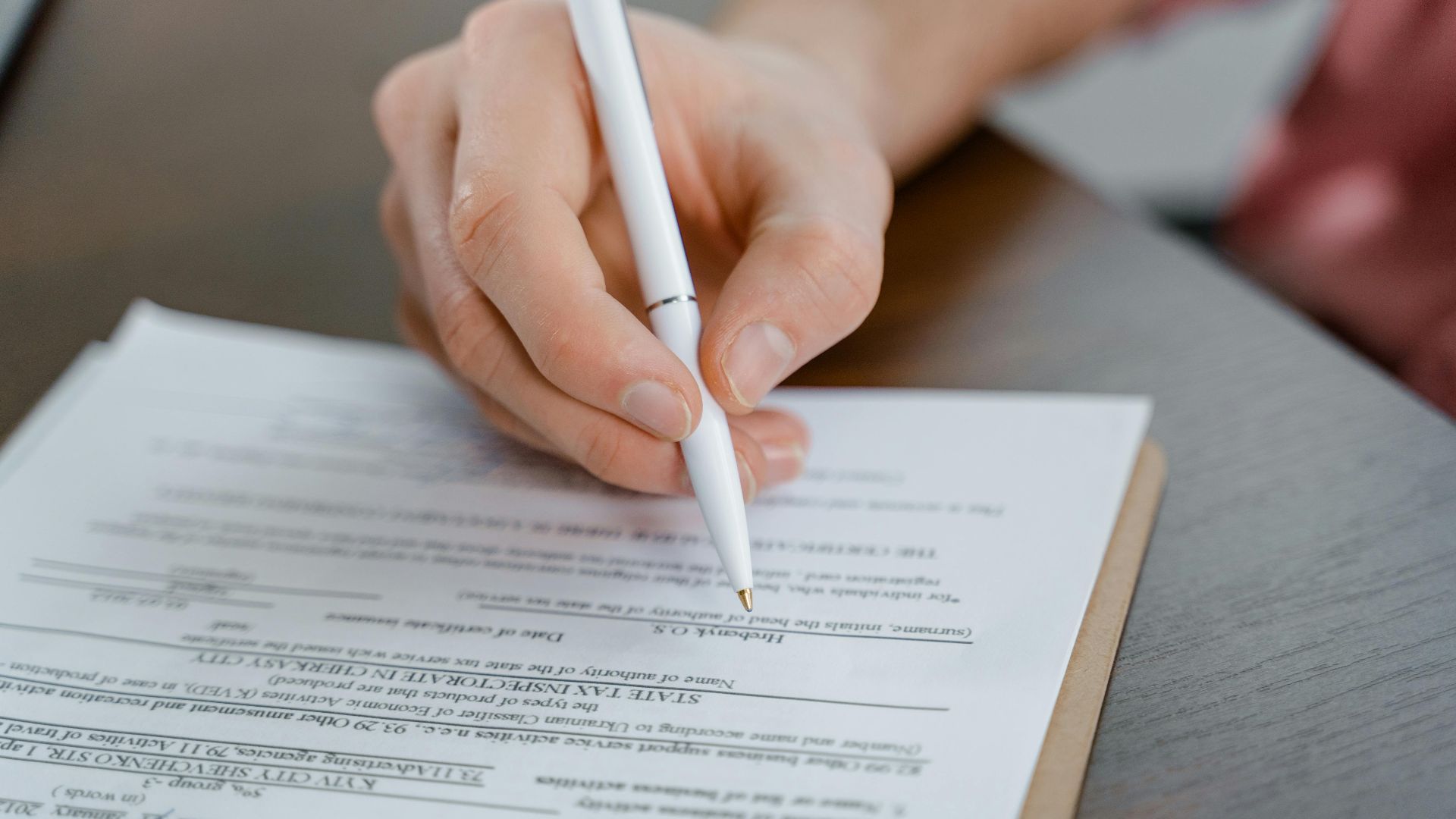 A hand holding a pen signing a document, close-up shot with focus on the paper.