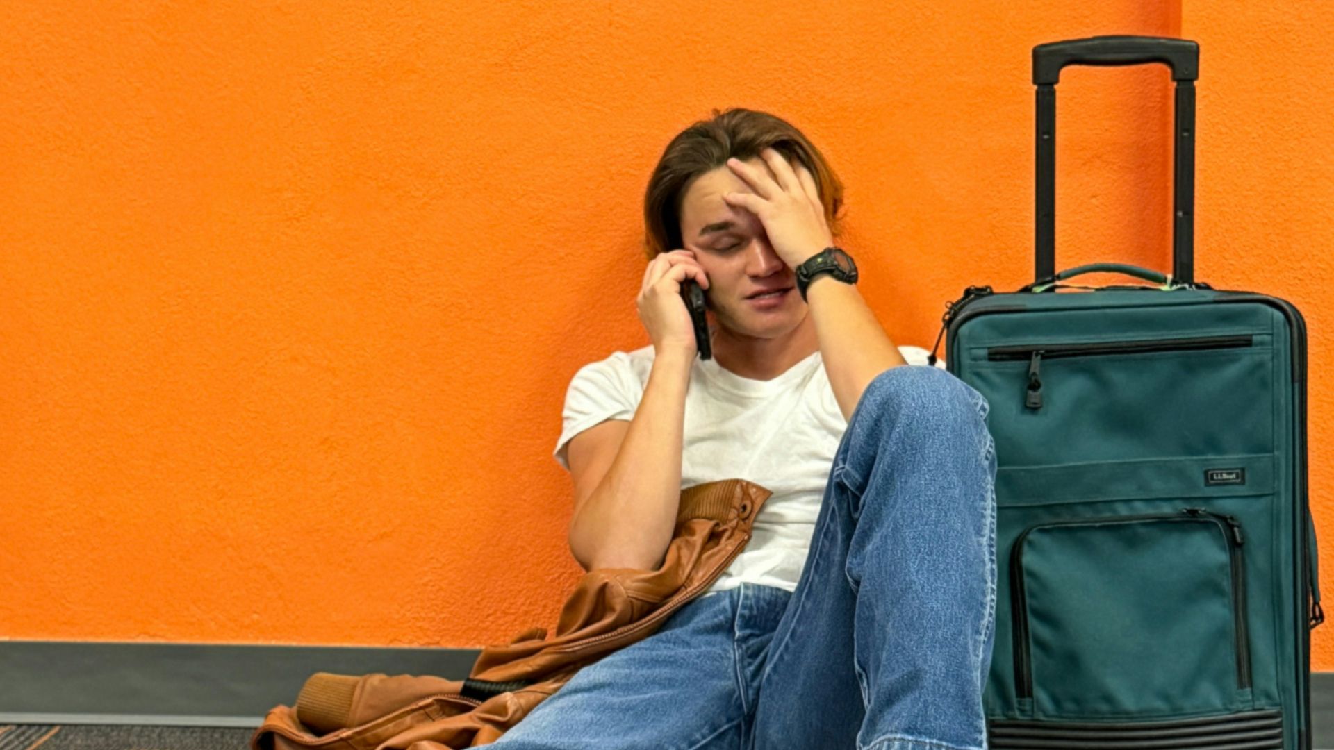 Man sitting on floor with suitcase, looking distressed.