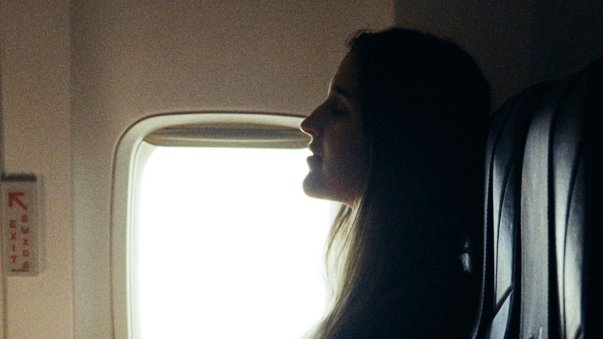 A woman relaxes on an airplane, sitting by the window during a daytime flight.