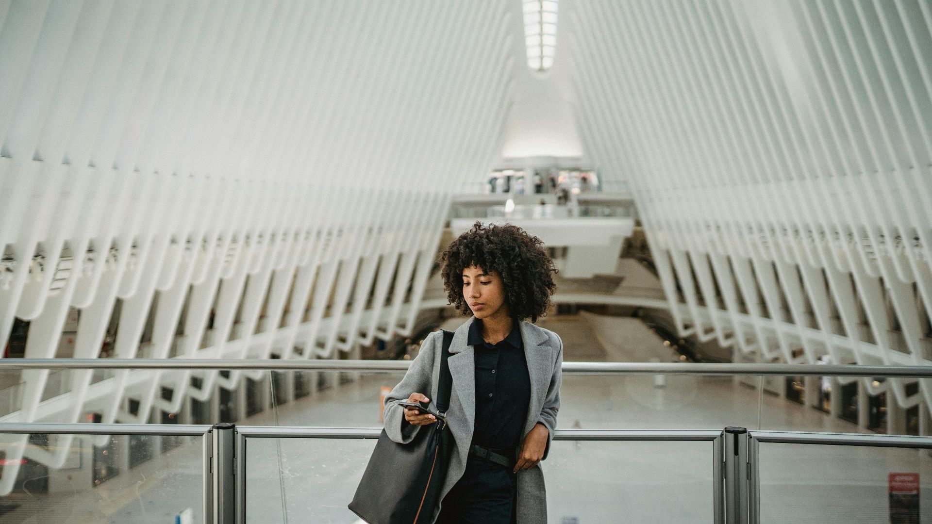 A fashionable woman with curly hair using a smartphone in a modern architectural setting.