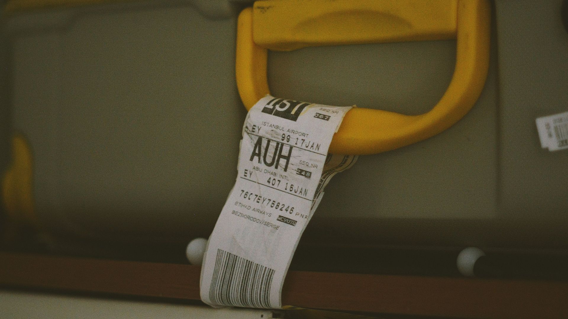 Close-up of a yellow suitcase handle with a visible travel tag and barcode, ideal for travel themes.
