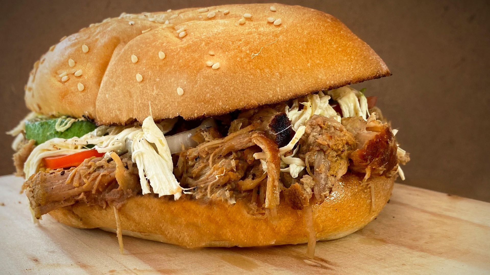 Mouth-watering close-up of a pulled pork sandwich with fresh ingredients and sesame seed bun.