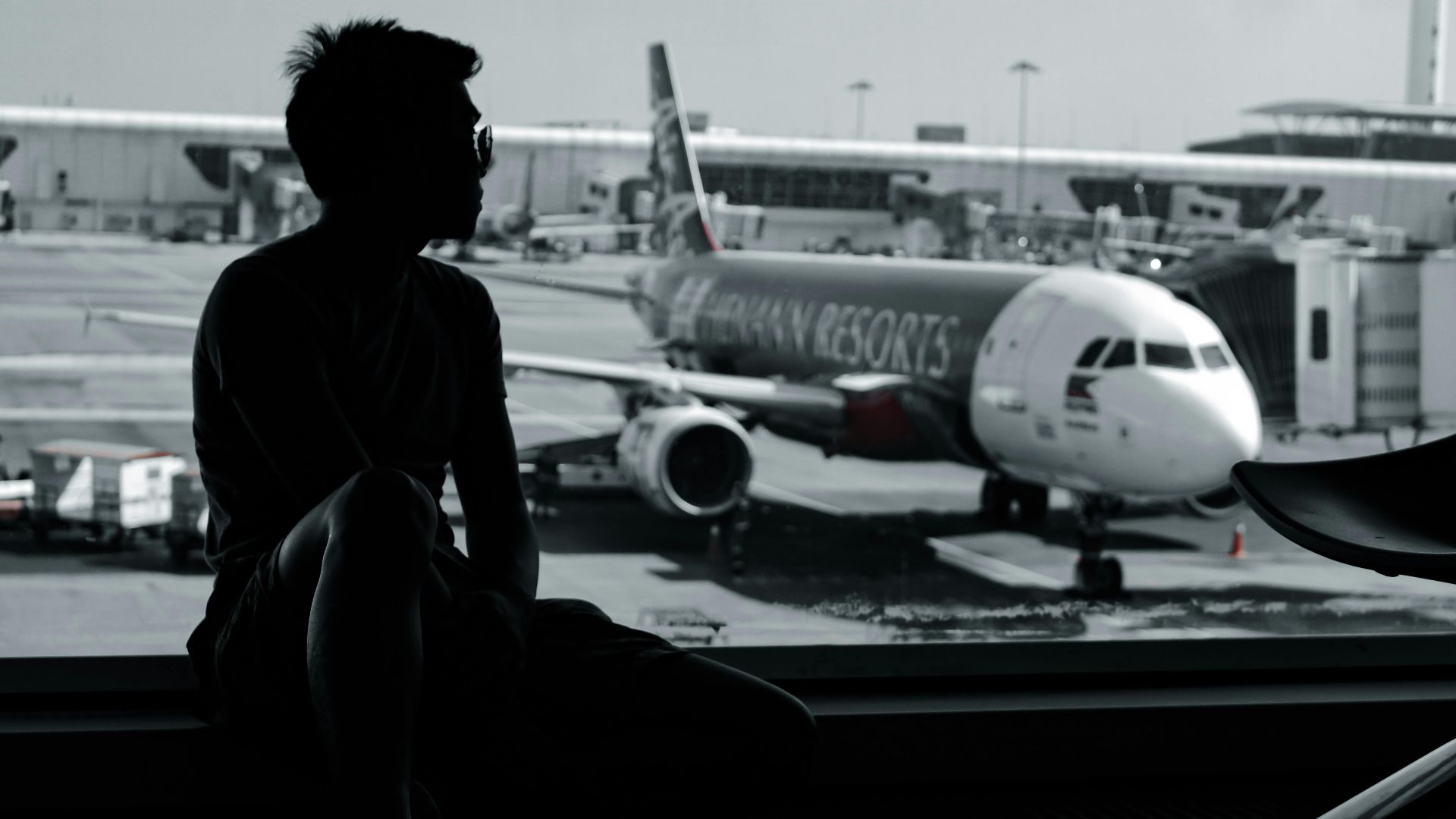 A silhouetted man sits in an airport terminal, viewing an airplane on the tarmac.