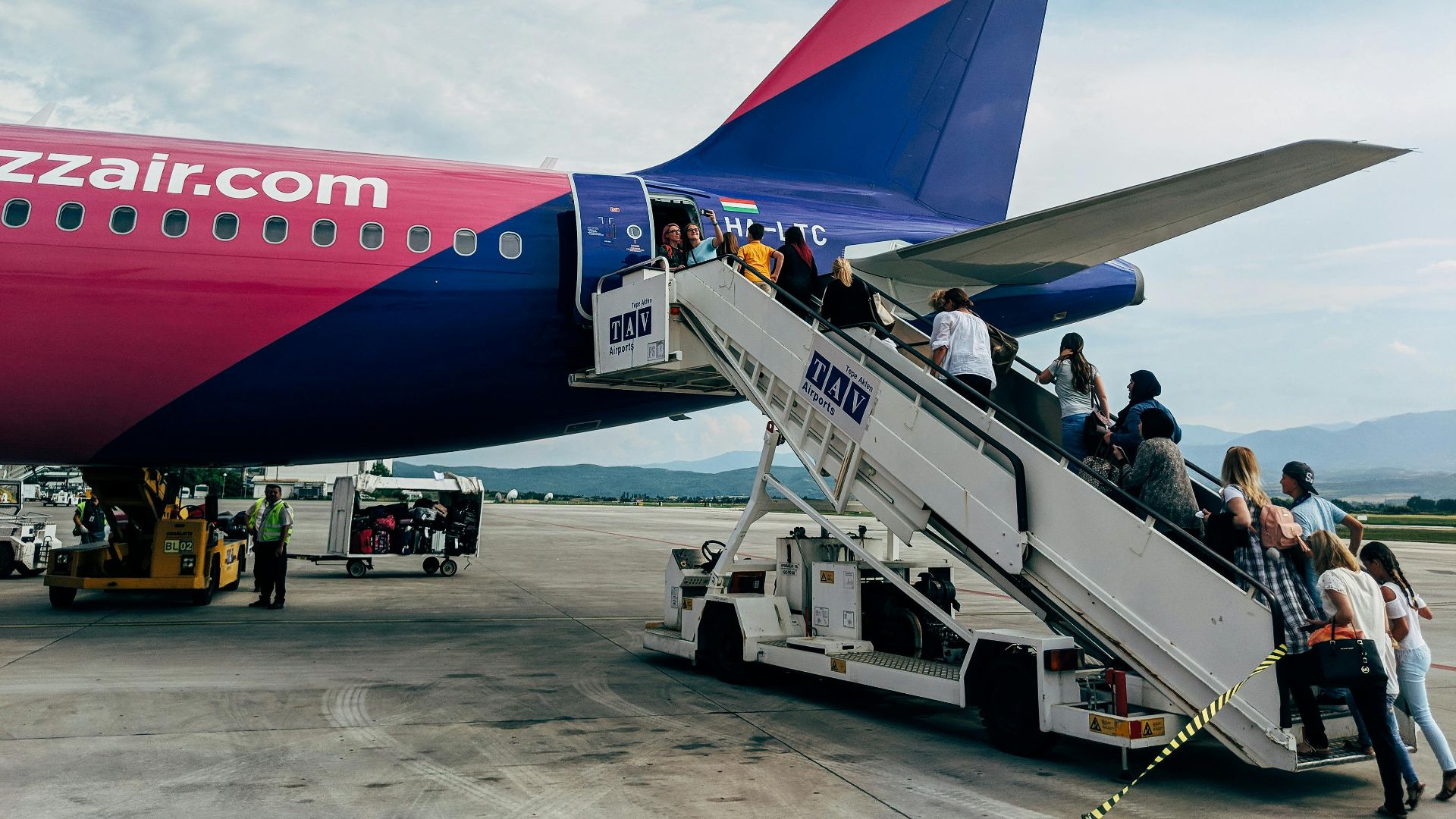 Travelers boarding a WizzAir Airbus A320 jet on a clear day at the airport.