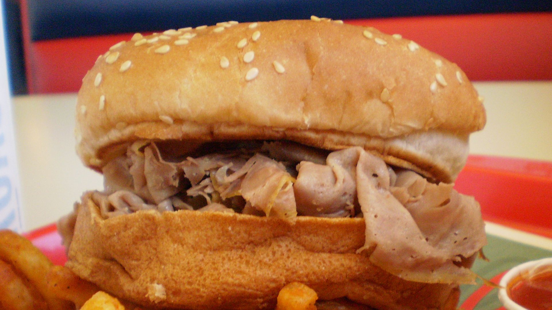 Arby's medium roast beef sandwich with curly fries and a small container of their special barbecue tangy something sauce. Entire bun shown.