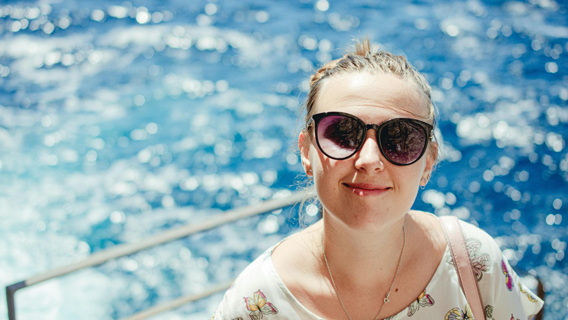 Smiling woman wearing sunglasses by the sparkling blue sea in Italy.