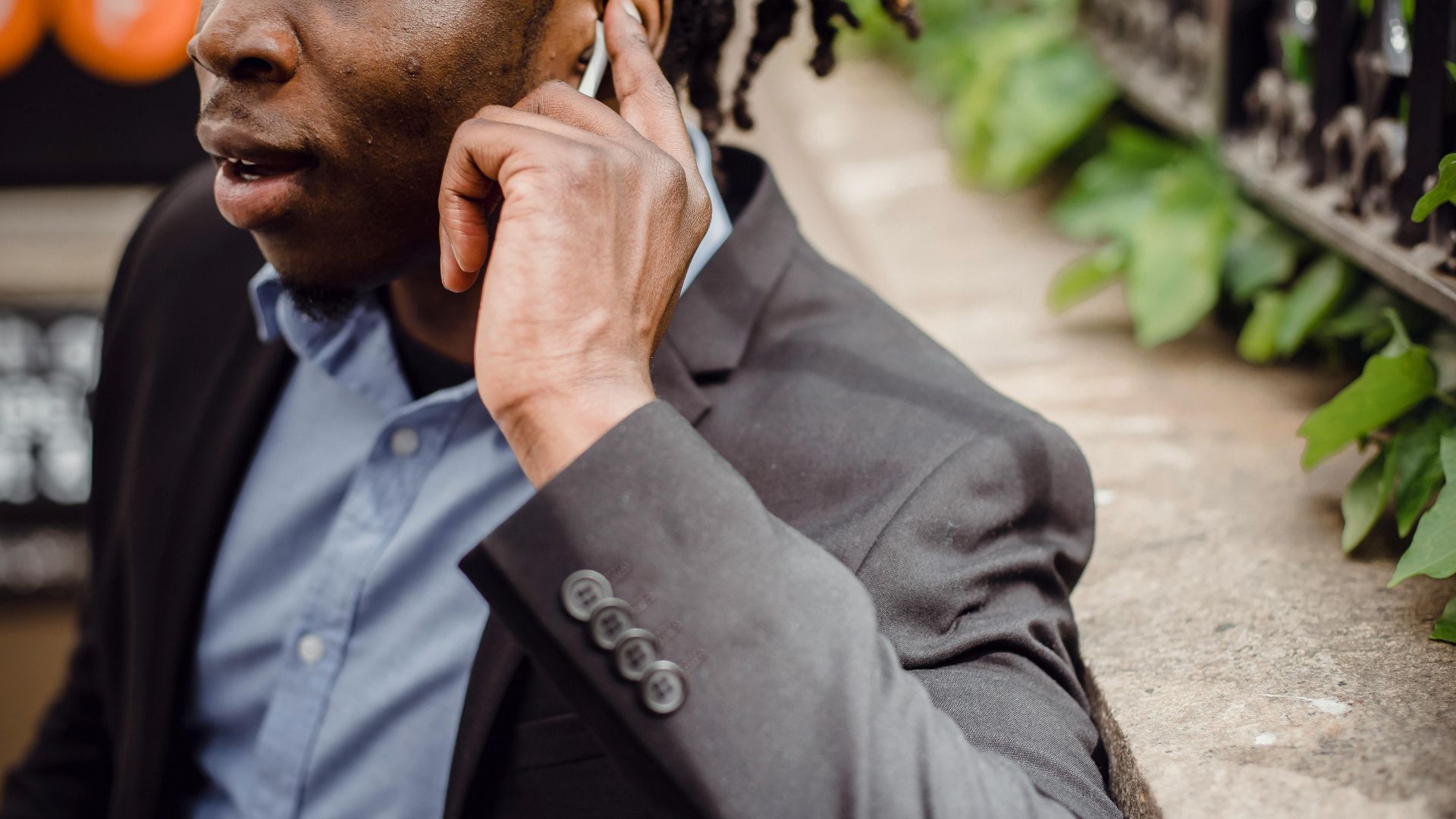 Crop well dressed black busy male having phone conversation and listening to interlocutor through wireless earbuds on street on summer day