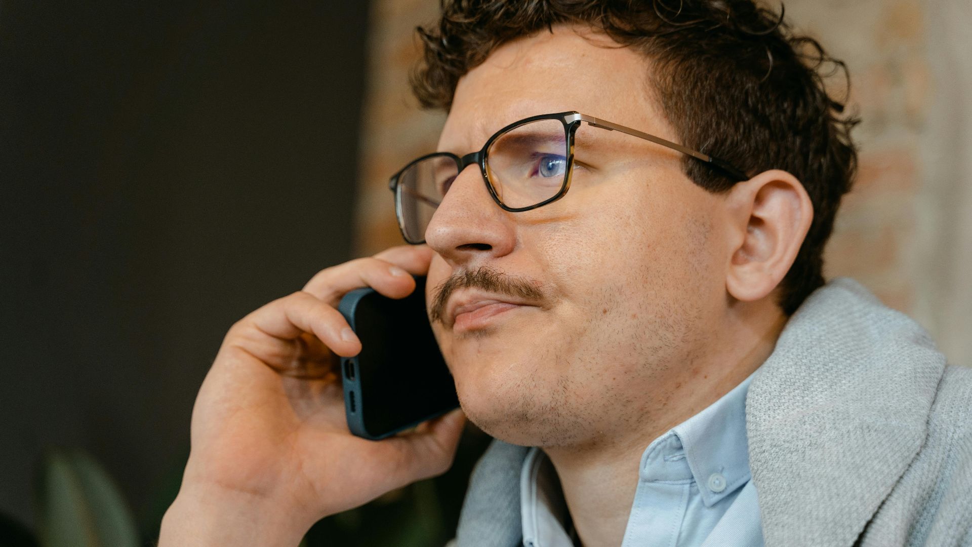 Man with glasses and mustache making a smartphone call indoors.