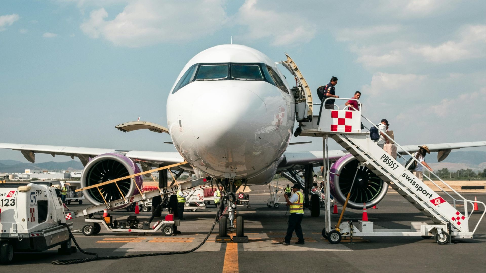 A large passenger airplane on the tarmac with boarding stairs and ground staff nearby.