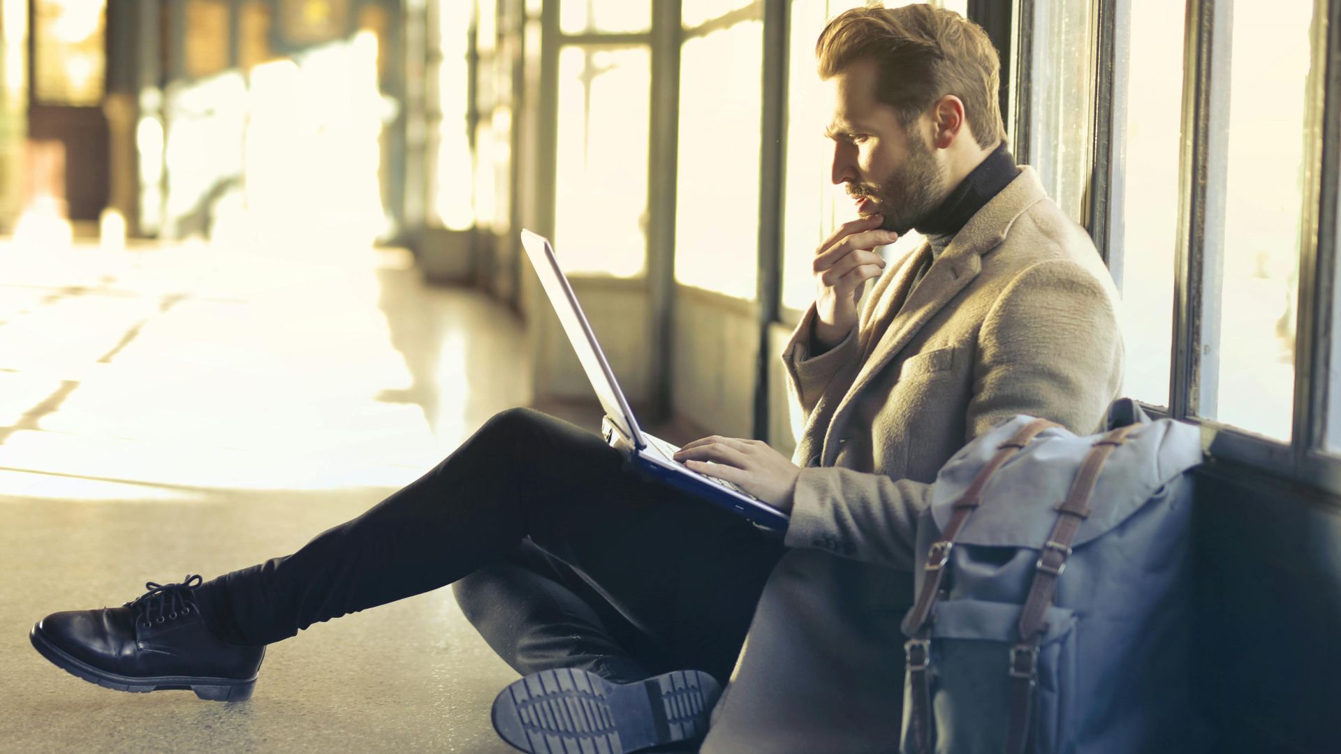 Young man sitting indoors at an airport using laptop. Ideal for remote work themes.