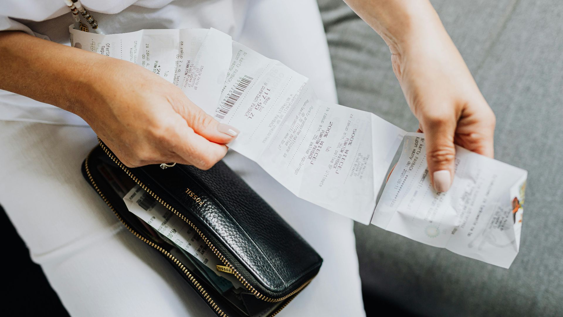 Close-up of a woman's hands managing multiple receipts taken from a black wallet.