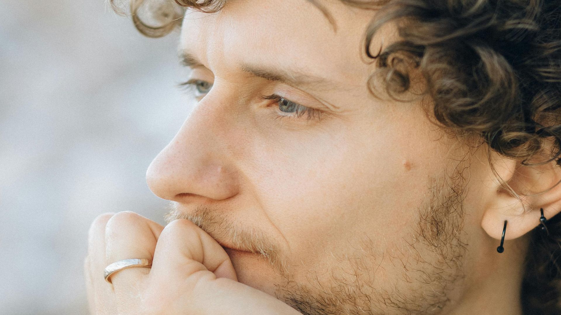 Close-up of a man with curly hair thoughtfully leaning on hand outdoors.