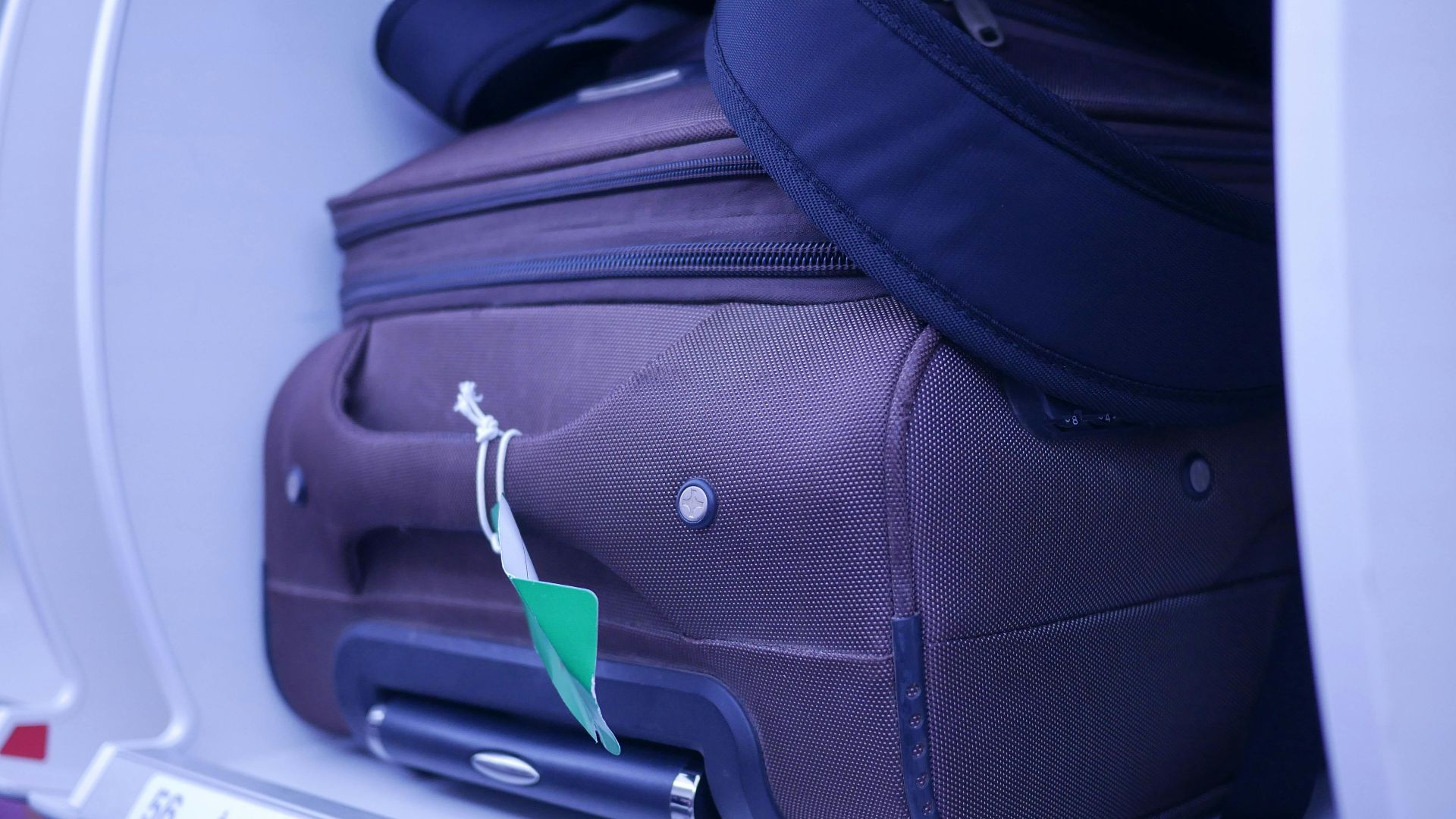 Close-up of luggage in an airplane's overhead compartment, showcasing travel essentials.