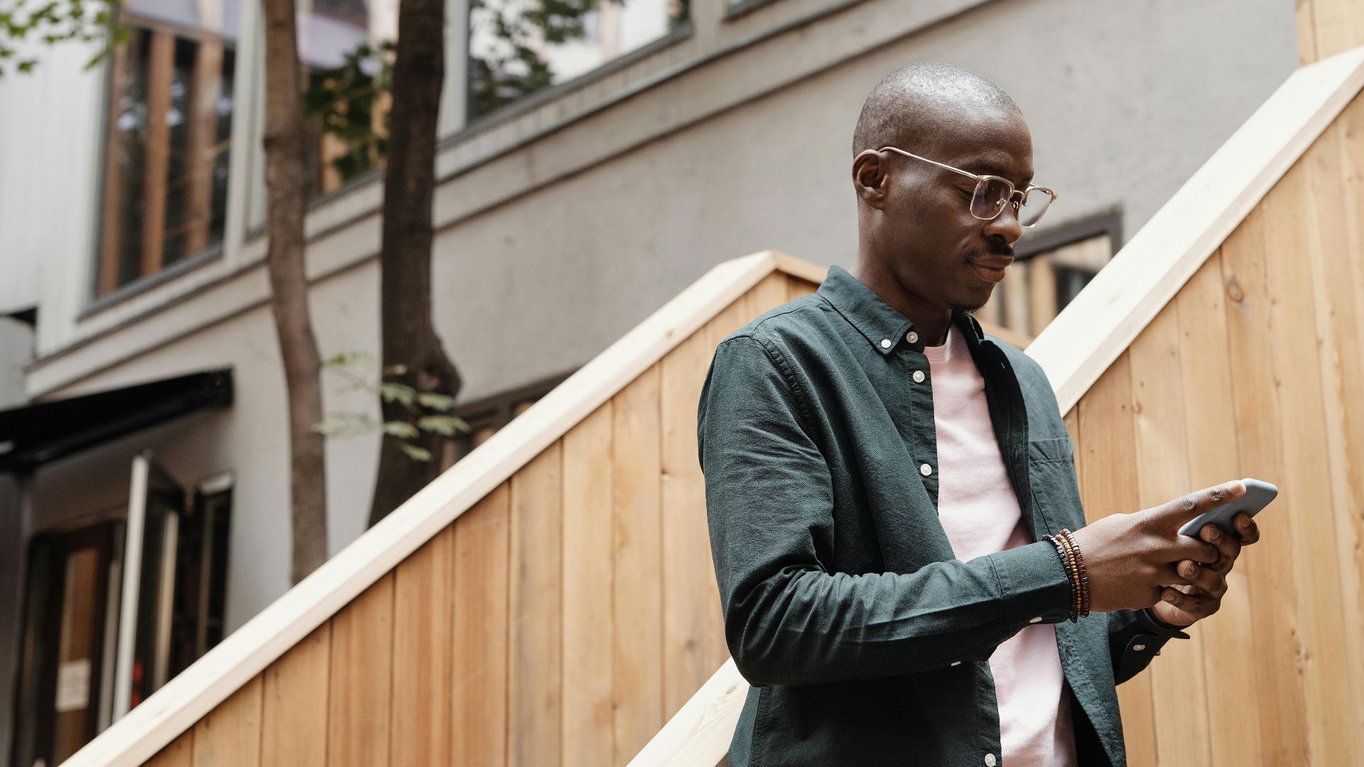 African American man texting on smartphone outdoors wearing stylish eyeglasses.